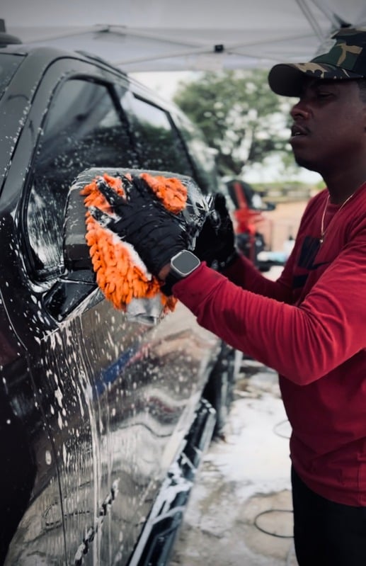 Owner applying a foam mitt to the side of a black car mid-wash